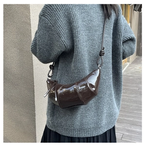 Detail of a glossy dark brown leather croissant bag with stylish knotted shoulder strap