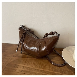 Detail of coffee brown patent leather crescent bag with knot strap on wooden desk