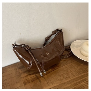 Detail of dark brown patent leather crescent bag with topstitching and knotted strap