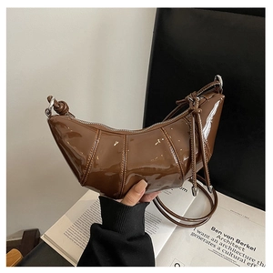 Detail view of brown glossy patent leather hobo bag with quilted design held by model