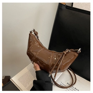 Close-up of brown patent leather moon bag with quilted stitching and knot handle detail