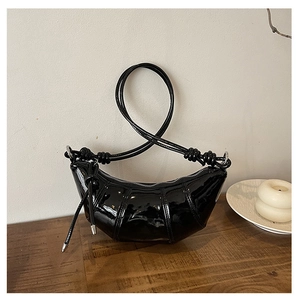 Detail of black glossy patent leather croissant bag with knotted shoulder strap and buckle