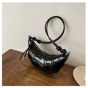 Detail of black glossy patent leather crescent bag with stylish knot strap and silver zipper