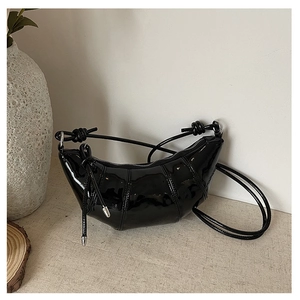 Close-up of black patent leather croissant bag with glossy mirror finish and metal zipper