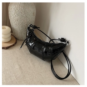 Detail of glossy black patent leather crescent bag with stylish knotted strap design