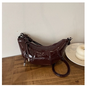 Detail of burgundy patent leather croissant bag with quilted pleats on a wooden surface