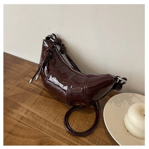 Macro shot of dark burgundy patent leather crescent bag with glossy texture and knotted strap