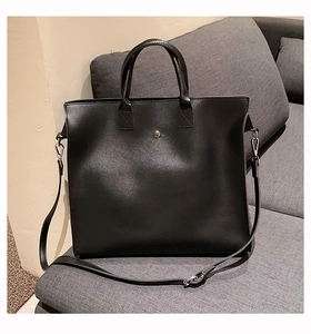 Dettaglio della borsa tote in pelle nera con bottone argento su un divano grigio
