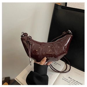 Detail of burgundy patent leather crescent bag featuring textured pleats and knot strap