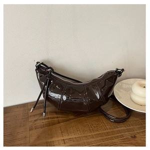 Detail of deep brown patent leather croissant bag with stylish side knot and silver zipper