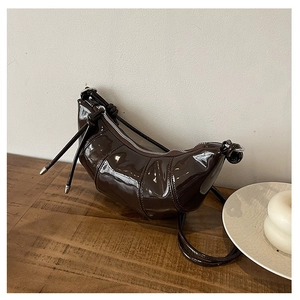 Detailed view of dark coffee patent leather croissant bag with knotted strap and metal trim