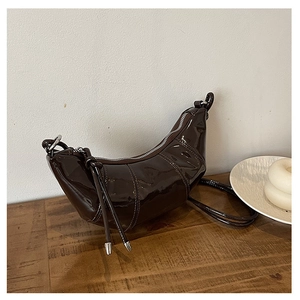 Detail of dark brown patent leather crescent bag with elegant pleats and long tassel zipper