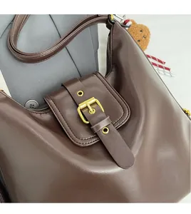 Detail of dark brown leather tote with large gold buckle and cute plush bear charm