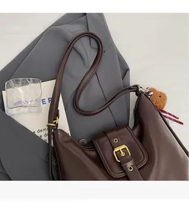 Close-up of a large brown leather hobo bag with a decorative buckle and a knit bear charm