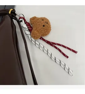 Close-up of a brown fluffy bear charm and woven rope hanging on a dark leather bag