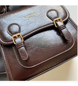 Detail view of brown oil wax leather bag featuring golden buckles and embossed logo