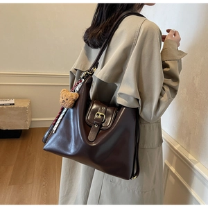 Brown leather tote bag featuring a cute teddy bear charm and adjustable shoulder strap
