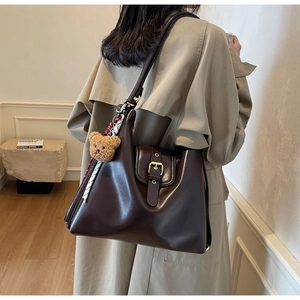 Deep brown large tote bag in soft leather shown on shoulder with plush bear charm