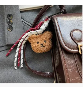 Close-up of brown plush bear pendant with braided rope tassel on a coffee leather bag