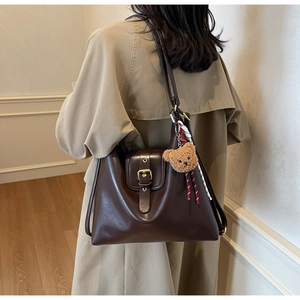 Detail of dark brown leather tote bag with brass buckle and plush bear charm on model