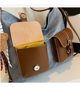 Detail of blue denim tote bag featuring brown leather pockets and a small plush bear charm