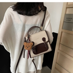Detail view of the contrast color handbag featuring a bear charm and fashion logo print
