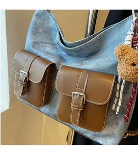 Detail view of denim tote bag with brown leather pockets and a small plush bear pendant