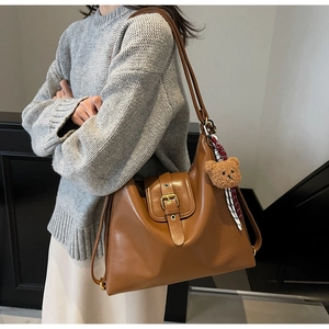 Detail of vintage brown tote bag featuring golden buckle and cute plush bear charm
