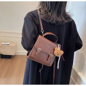 Rear view of a model wearing a brown vintage PU leather backpack with a bear pendant