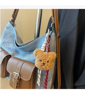 Detailed view of a brown plush bear charm with woven ropes on a denim leather bag