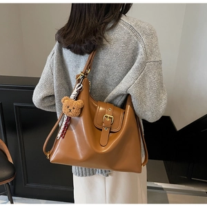 Close-up of brown leather tote bag with a plush bear charm and striped silk scarf accessory