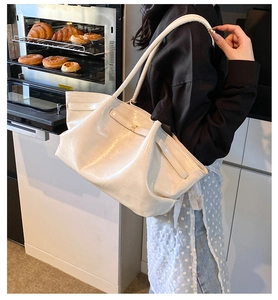 Creamy white pleated tote bag worn by a model in a cozy modern kitchen lifestyle setting