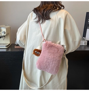 Sac bandoulière en peluche rose avec breloque poupée porté par un mannequin en café