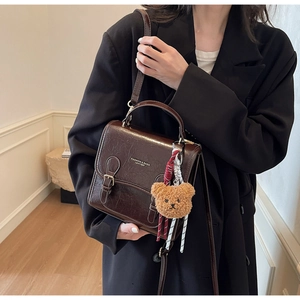 Detail of dark brown vintage faux leather handbag with plush bear charm and gold text