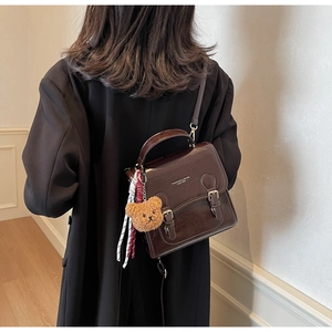 Detail of dark brown retro shoulder bag featuring double buckle and plush bear charm accessory