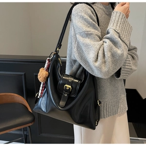 Detail of a large black leather hobo bag with a plush bear charm and striped scarf detail