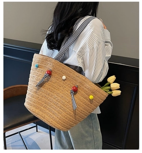 Detail of woven straw tote bag with colorful pom-poms and striped shoulder strap