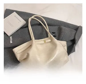 Detail of off-white pleated tote bag with glossy texture and elegant gold buckles