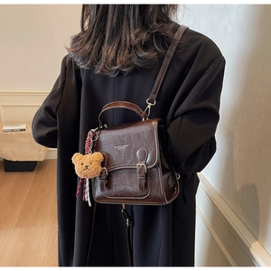 Detailed view of dark brown vintage leather backpack with plush bear and striped strap