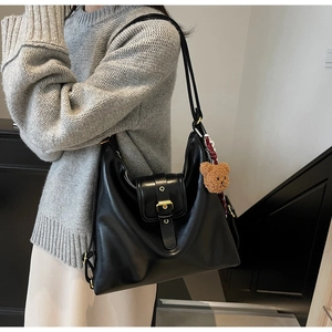 Detail of black faux leather tote bag with metallic buckle and cute bear plush charm