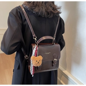 Detail of a dark brown glossy leather backpack with a plush bear charm on a model's back