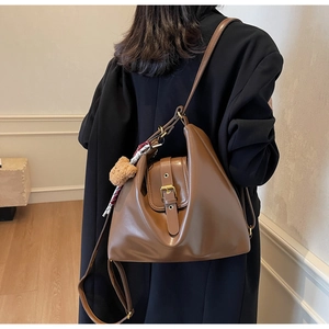 Detail of a brown leather hobo bag with vintage buckle and bear charm accessory