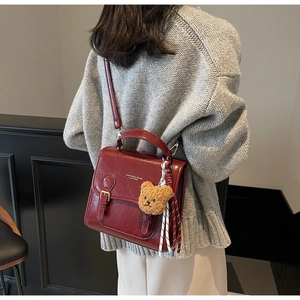 Detail of burgundy leather shoulder bag with double buckles and a brown teddy bear charm