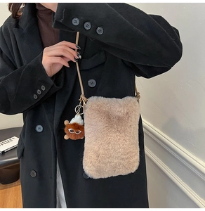 Détail d'un sac de téléphone en peluche marron clair avec charm mignon sur un manteau noir