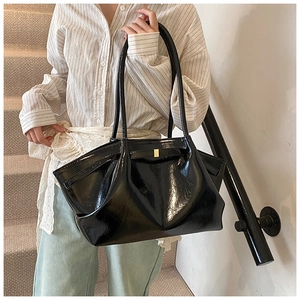 Close-up of black glossy pleated tote bag with golden metal buckle and thin shoulder straps