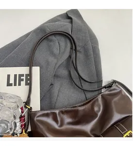 Detail of brown leather hobo bag featuring white stitching and gold metal buckles