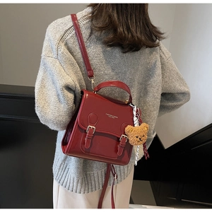 Deep red patent leather backpack with golden lettering and a cute bear charm detail