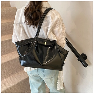 Close-up of black glossy pleated tote bag with golden buckle on urban stairs
