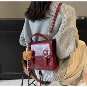 Detailed view of burgundy vintage leather handbag featuring a plush bear charm on model