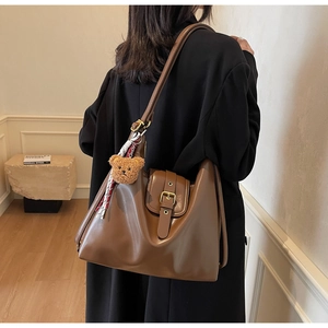 Detail of a brown leather tote bag with flap closure and cute bear pendant accessory